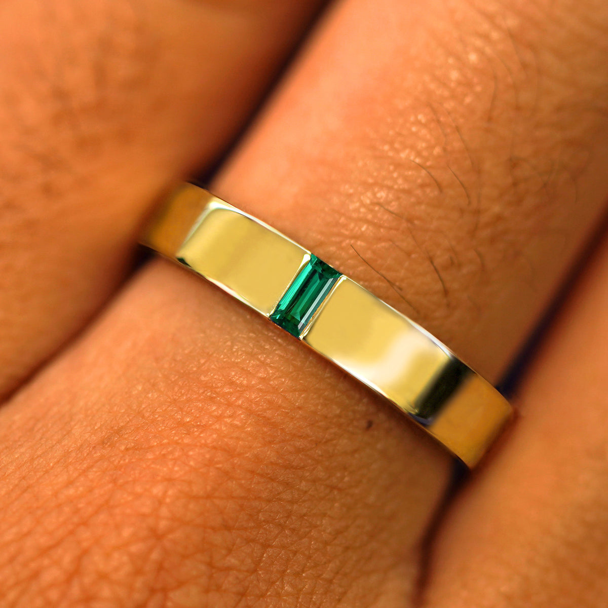 Close up view of a model's hand wearing a solid yellow gold Lab Emerald Baguette Band