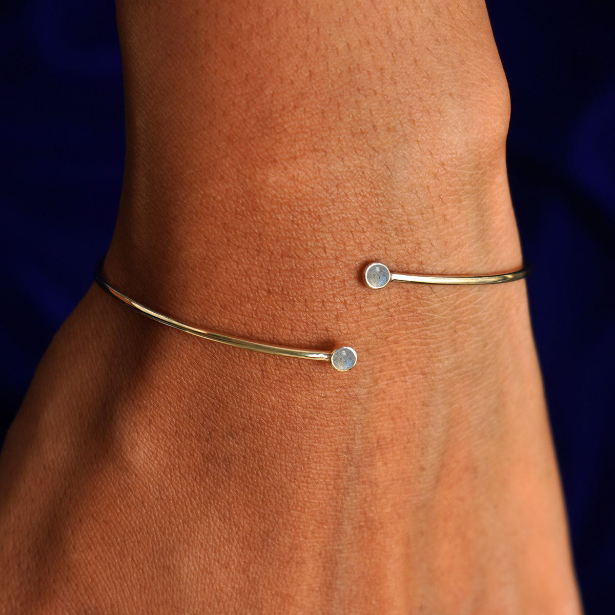 Close up view of a model's wrist wearing a 14k gold labradorite gemstone bypass bangle