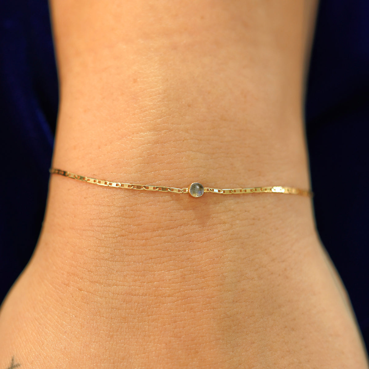 A model's wrist wearing a solid 14k yellow gold Labradorite Bracelet