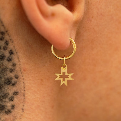 A photo of a model wearing huggie hoop with large open 8 pointed star charm