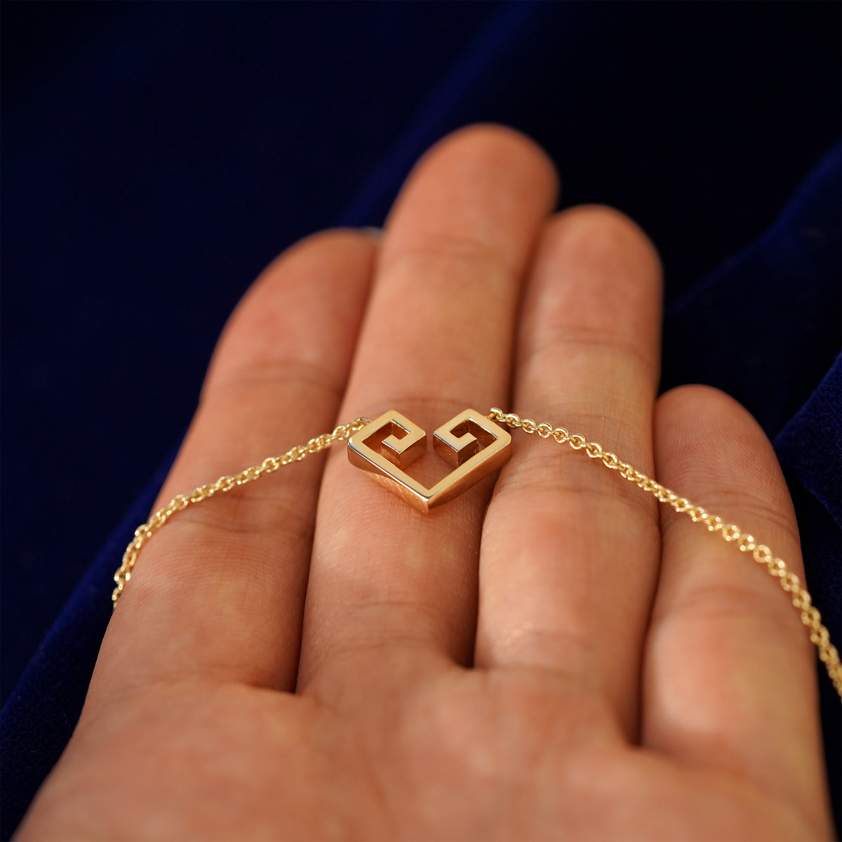 A 14k gold large geometric heart necklace resting on a model's fingers