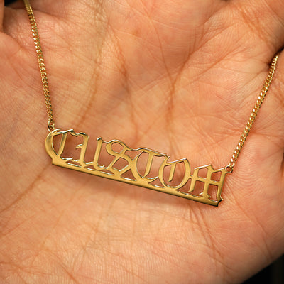A 14k yellow gold custom nameplate necklace resting in a model's palm