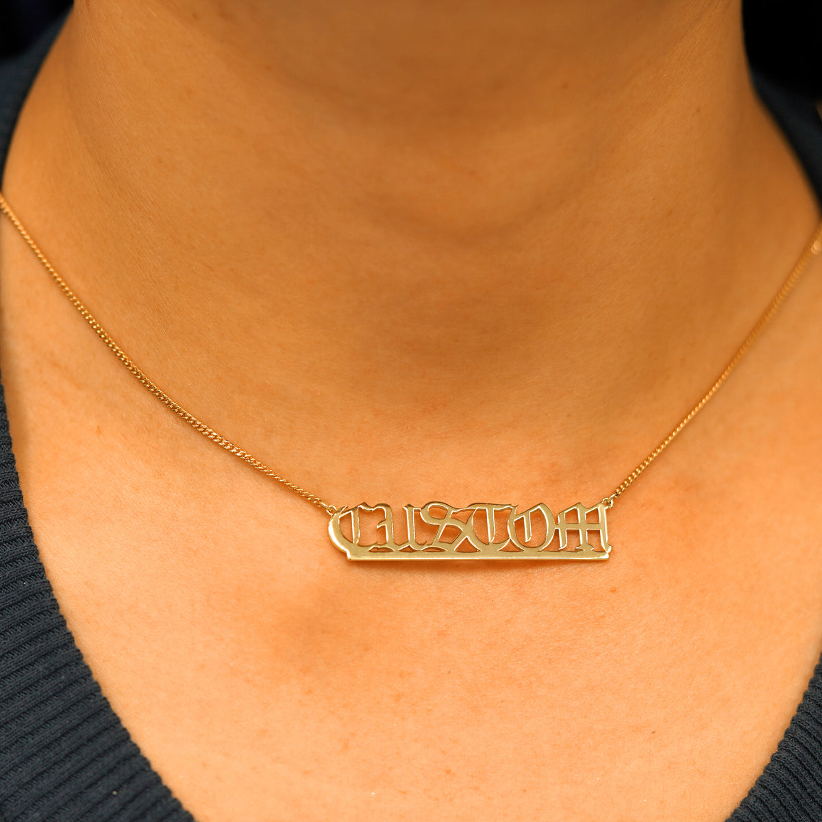 A model's neck wearing a Large Custom Nameplate necklace that reads the word Custom