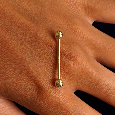 A yellow gold Large Straight Barbell Piercing resting on the back of a model's hand