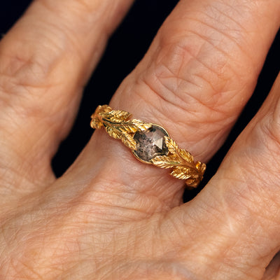 Close up view of a model's fingers wearing a 14k yellow gold Salt and Pepper Diamond Leaves Ring