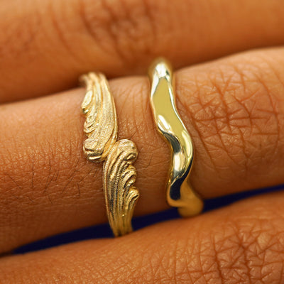 A model's hand wearing a yellow gold Liquid Band and a Waves Band stacked