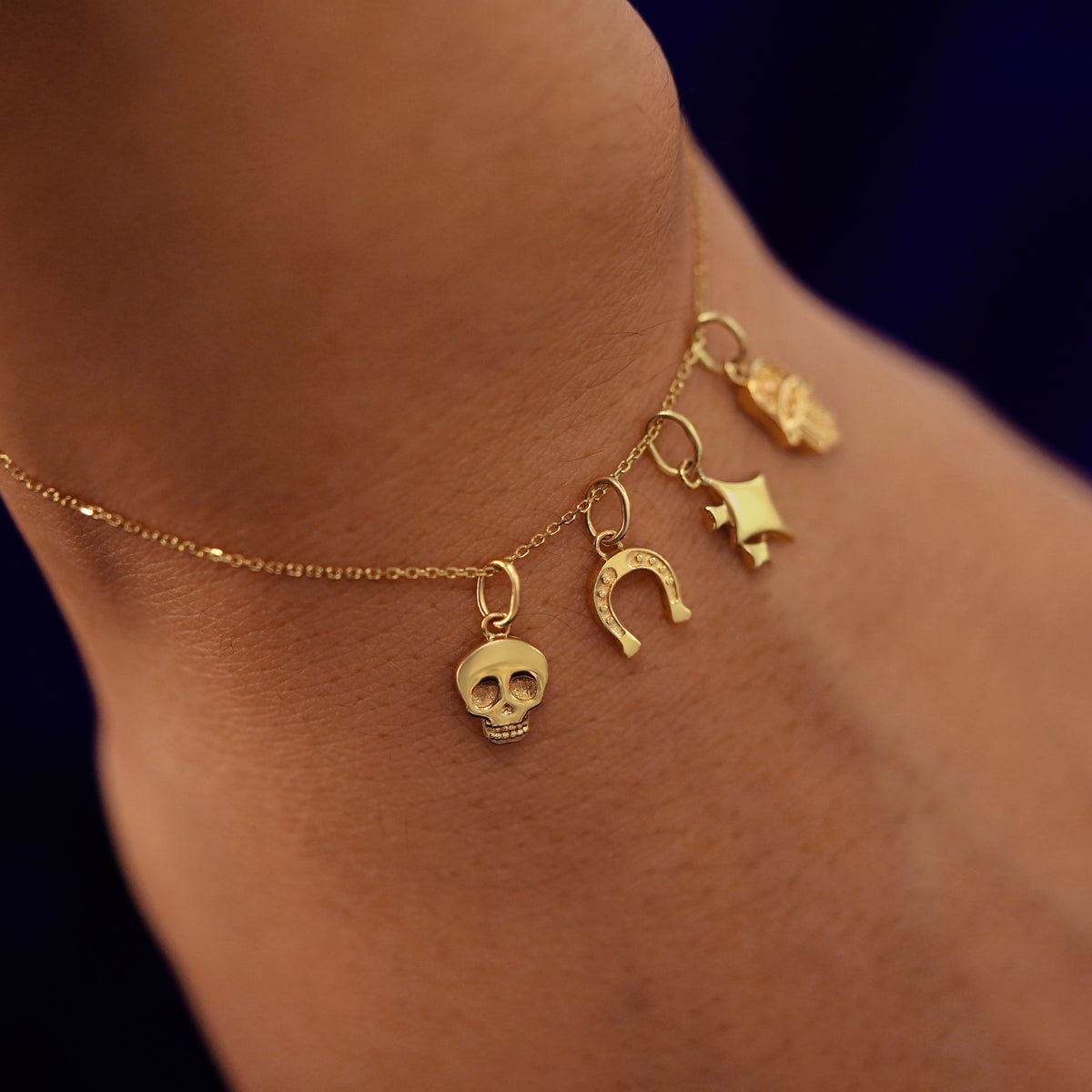 Close up view of a model's wrist wearing skull, horseshoe, sparky emoji, and hamsa charms on a cable bracelet