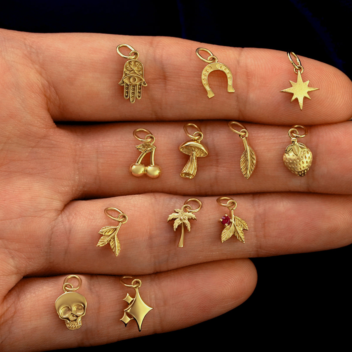 Close up view of a model's hand holding various good luck and nature themed solid 14k gold charms