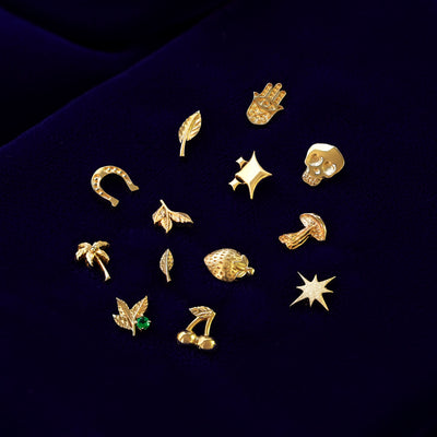 Various 14k yellow gold good luck and nature themed stud earrings on a dark blue cloth background