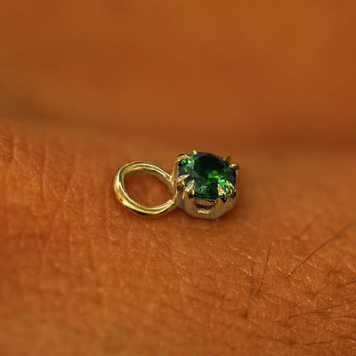 A solid yellow gold Emerald Charm for earring resting on the back of a model's hand