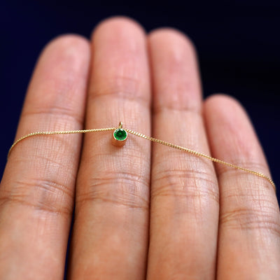 A 14k gold Emerald Necklace draped over a model's fingers