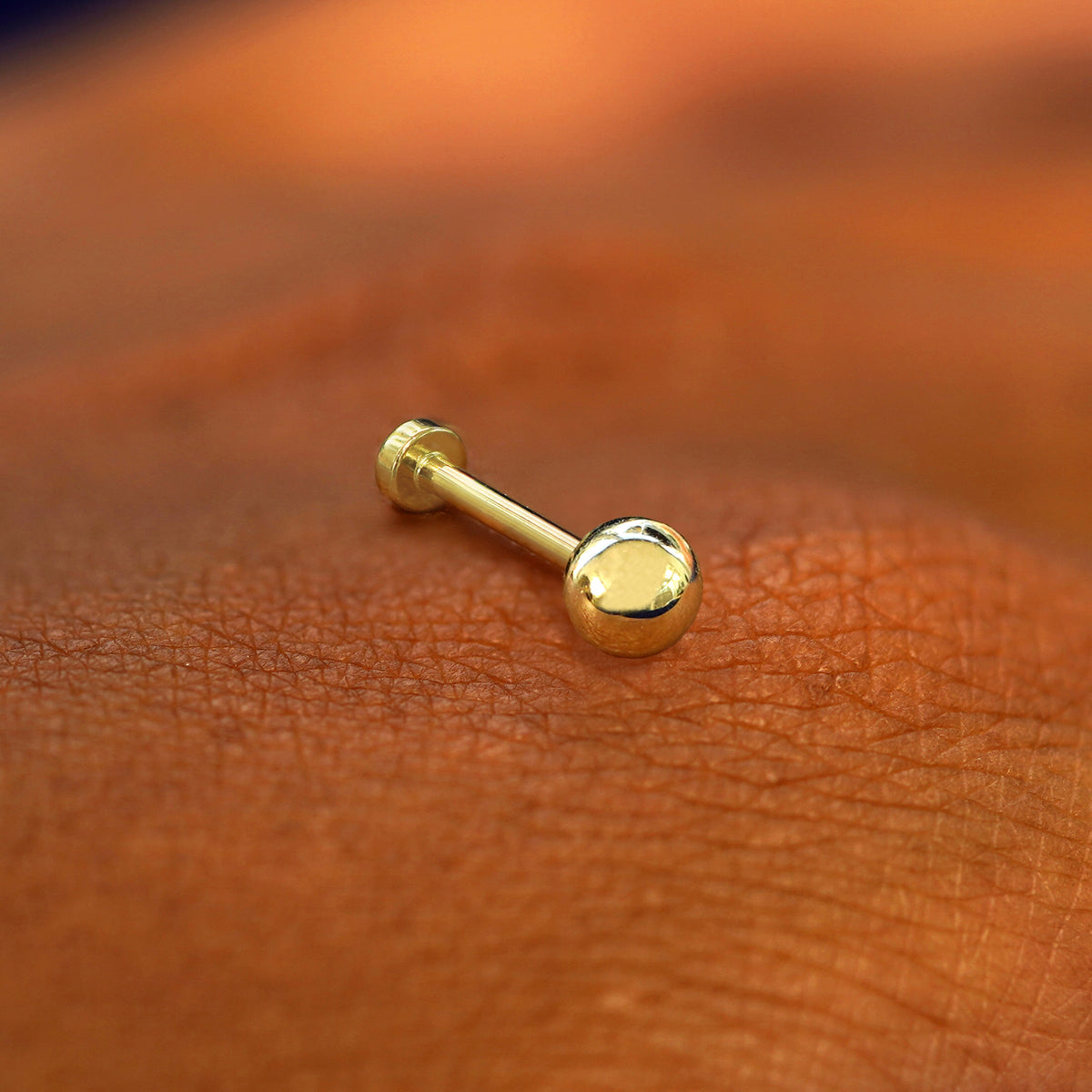 A yellow gold Medium Ball Flatback Piercing laying on the back of a model's hand