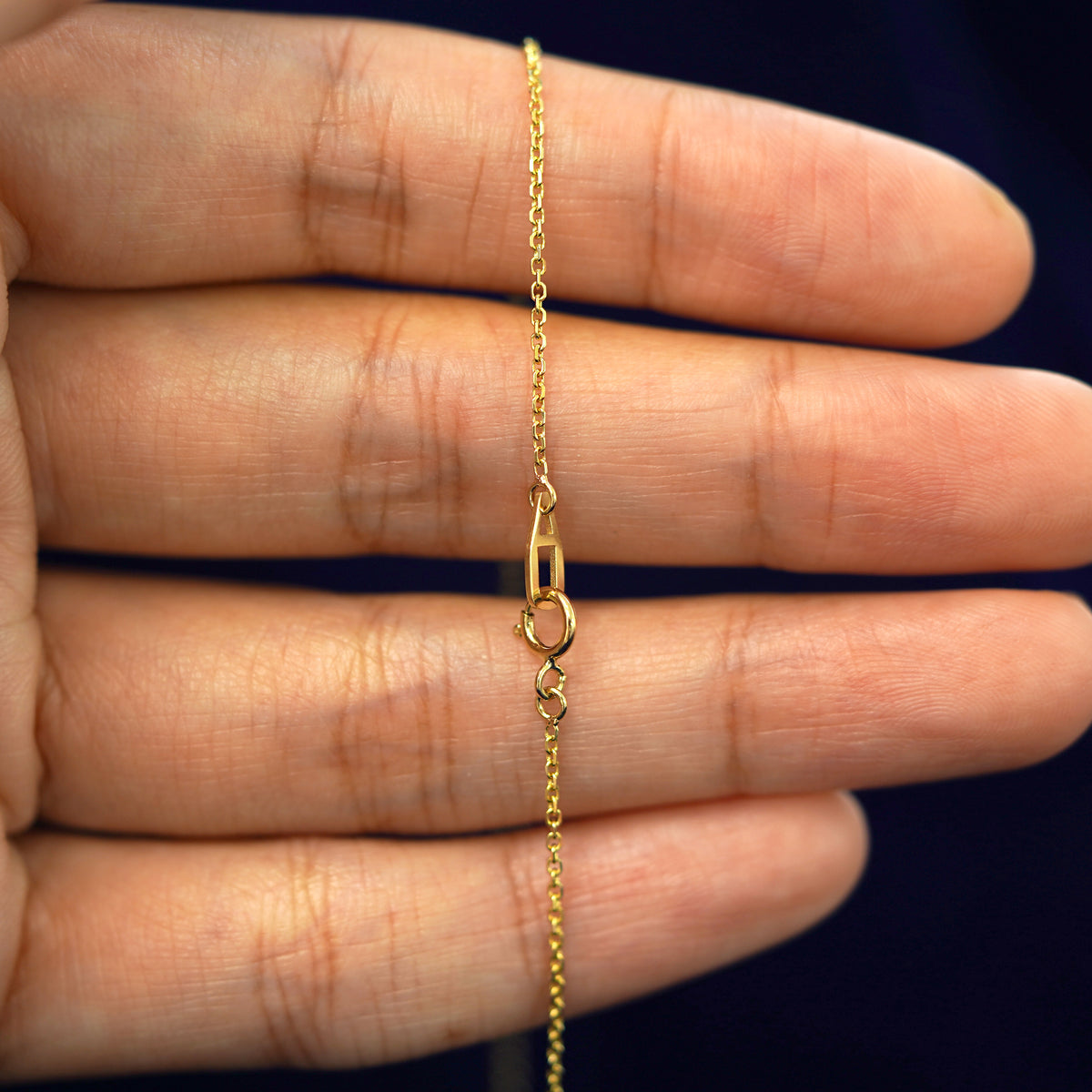 A model's hand holding a yellow 14k gold Medium Cable Chain with an Automic Gold AU spring ring lock