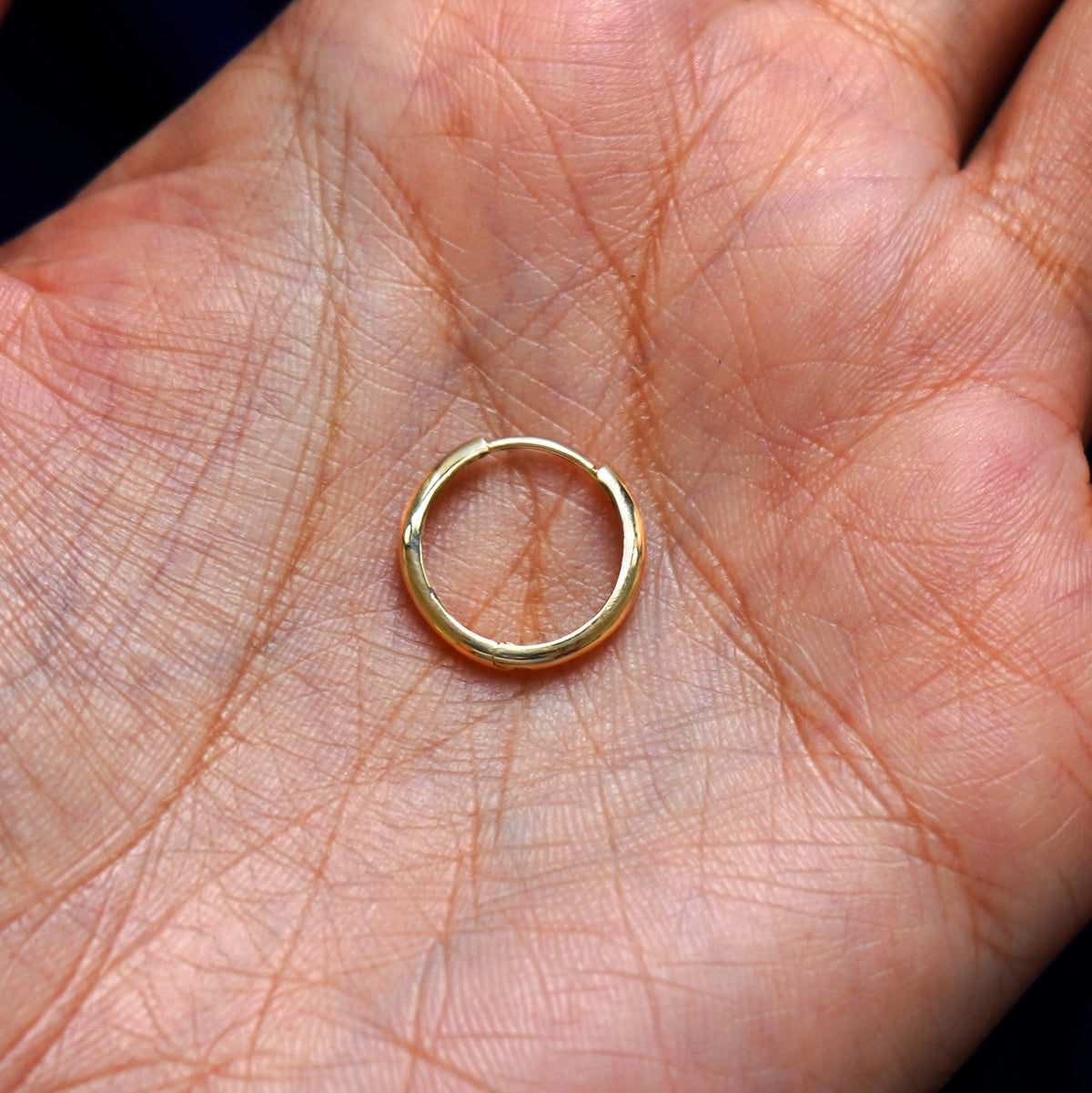 A solid 14k yellow gold Medium Curvy Huggie Hoop Earring closed in a model's palm