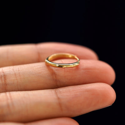 A yellow gold Medium Curvy Huggie Hoop Earring laying sideways on a model's fingertips