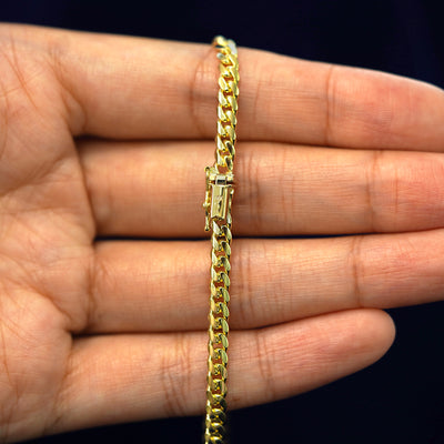 A model's hand holding a yellow 14k gold Medium Miami Chain with a box clasp