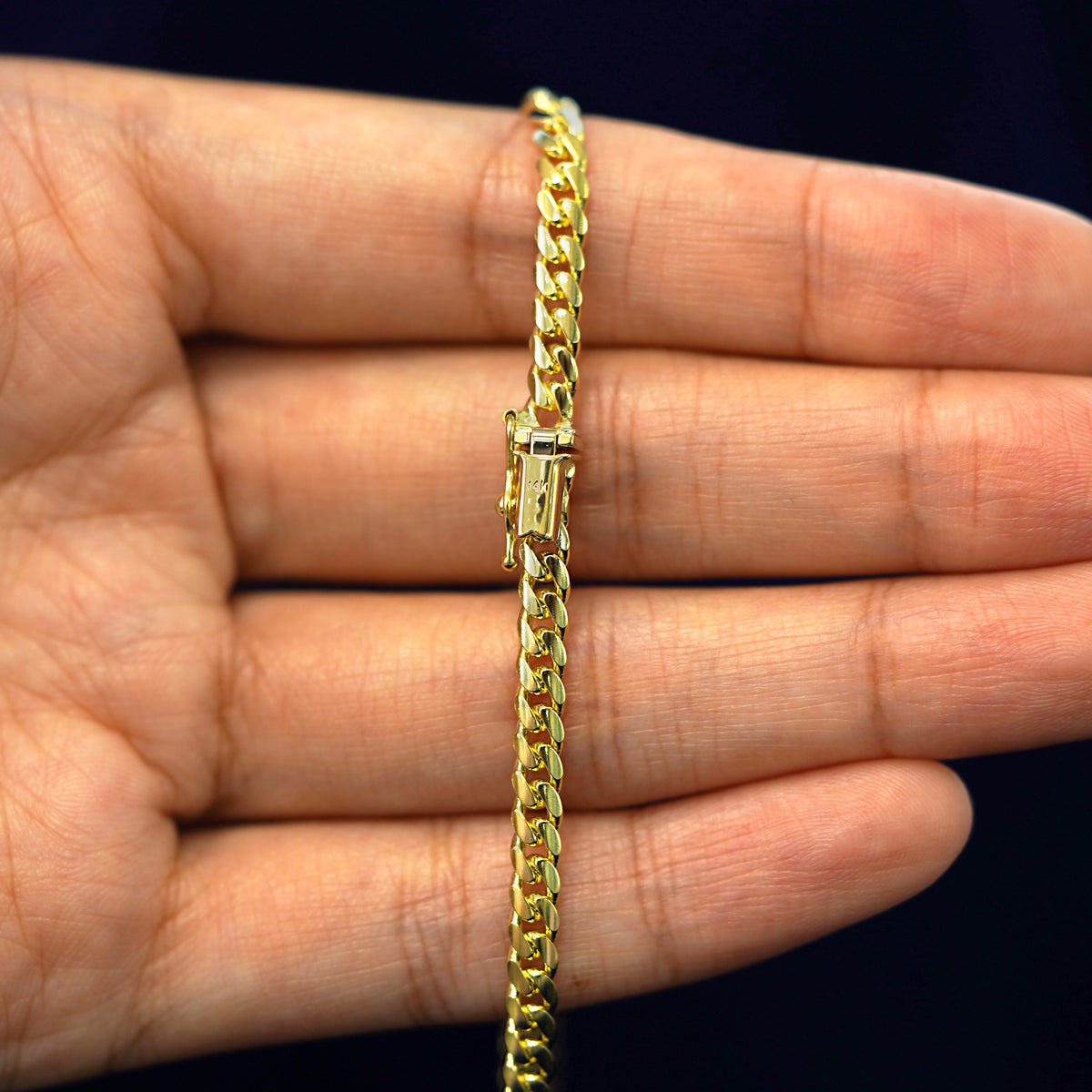 A model's hand holding a yellow 14k gold Medium Miami Bracelet with a box clasp