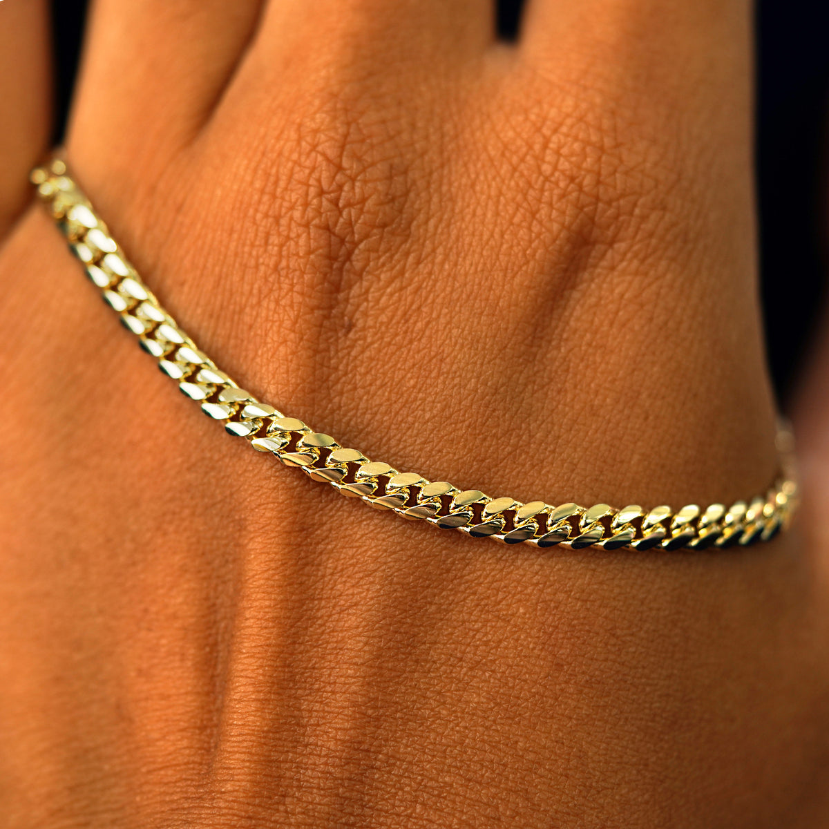 A solid gold Medium Miami Anklet resting on the back of a model's hand