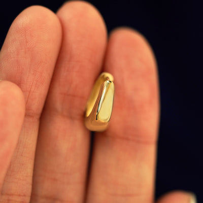 A 14k solid gold Medium Teardrop Huggie Hoop between a model's fingers to show the thickness of the earring