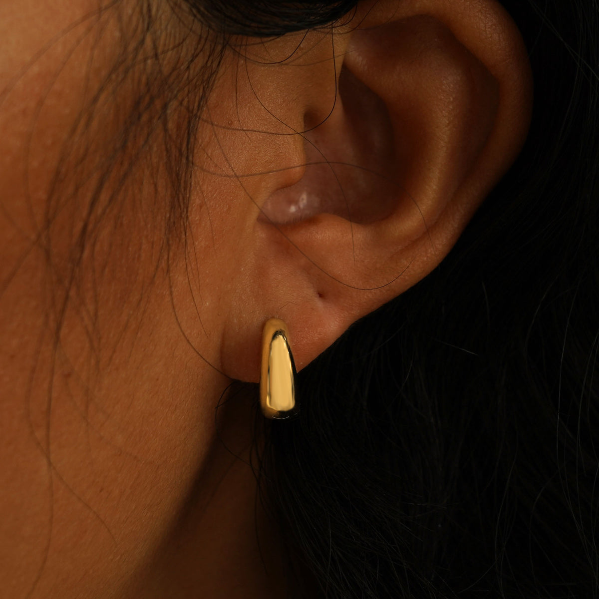 A model's ear wearing a  yellow gold Medium Teardrop Huggie Hoop and a Small Teardrop Huggie Hoop in two piercings