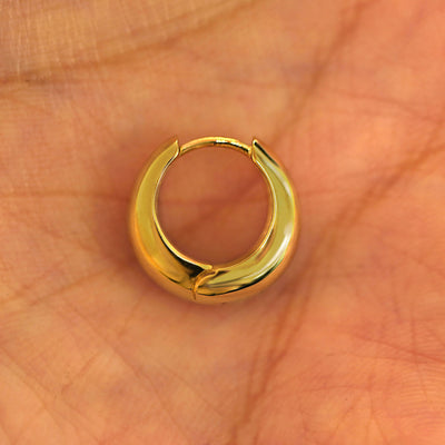 A single closed 14k yellow gold Medium Teardrop Huggie Hoop resting in a model's palm