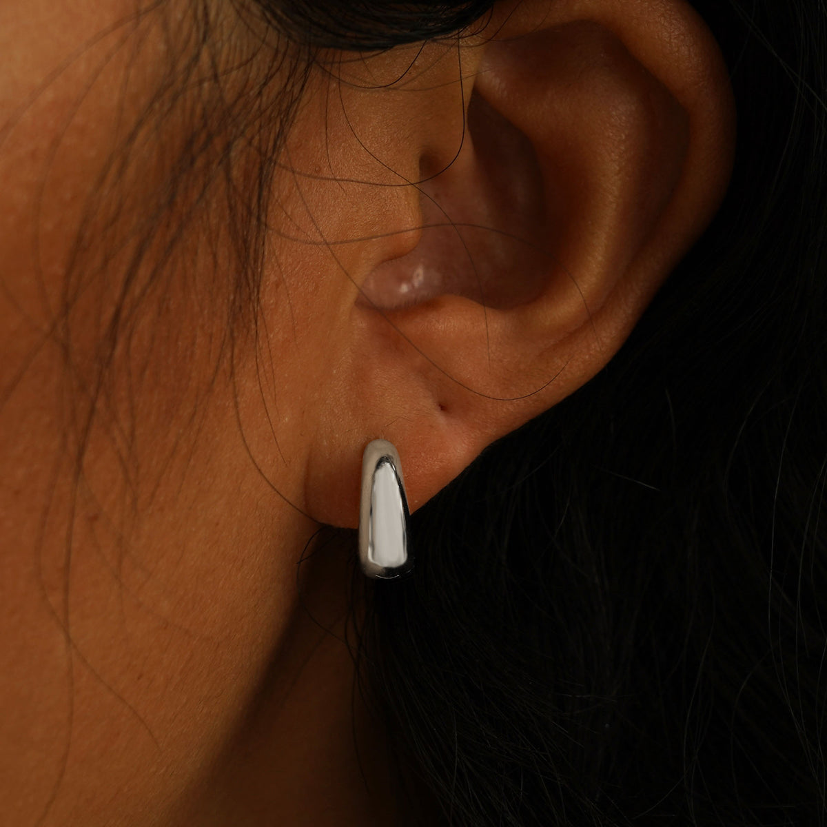 A model's ear wearing a white gold Medium Teardrop Huggie Hoop and a Small Teardrop Huggie Hoop in two piercings