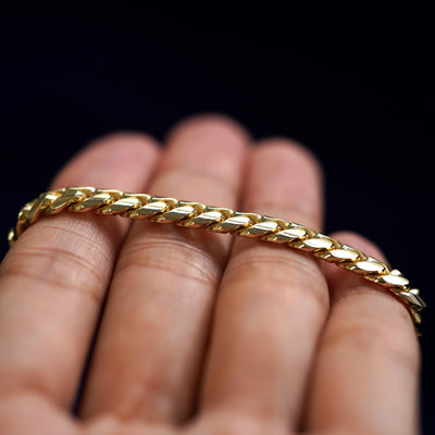 A yellow gold Miami Cuban Anklet resting on a model's fingers