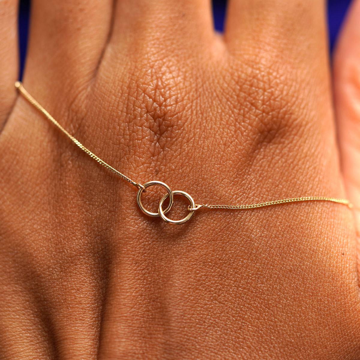 A solid gold Mini Bound Together Necklace resting on the back of a model's hand