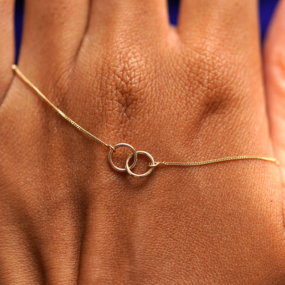 A solid gold Mini Bound Together Necklace resting on the back of a model's hand