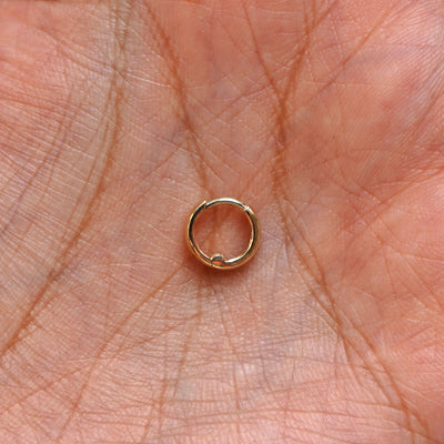 A solid 14k yellow gold Mini Thick Huggie Hoop Earring closed in a model's palm
