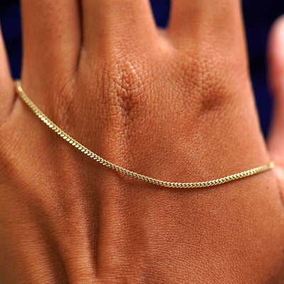 A solid gold Mini Miami Anklet resting on the back of a model's hand