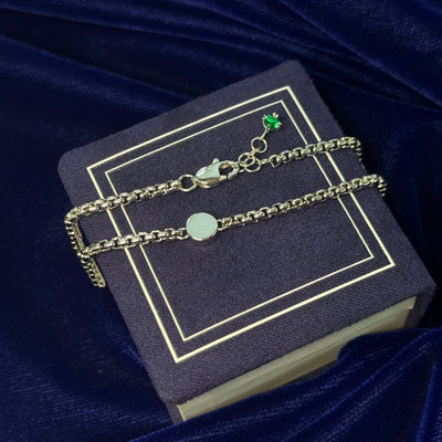 A photo of mirror circle necklace with sand inside resting on a blue background 