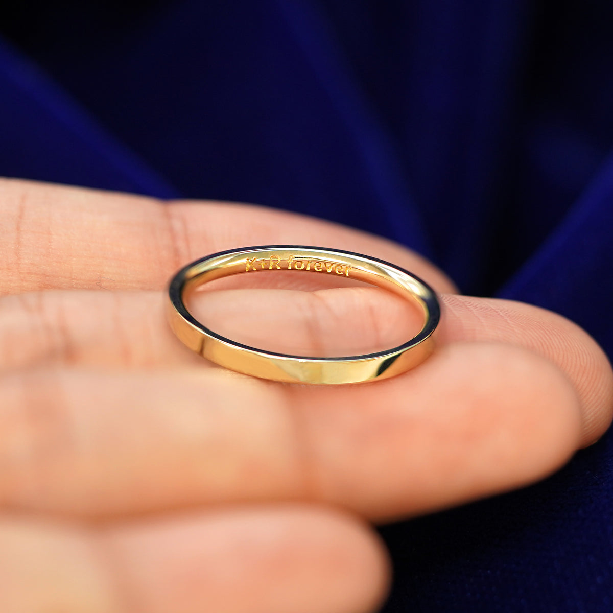 A Industrial Mirror Band in a model's hand tilted to show engraving on the inside of the band that reads K + R Forever