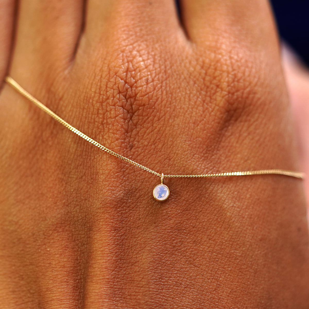 A solid yellow gold Moonstone Necklace draped across the back of a model's hand