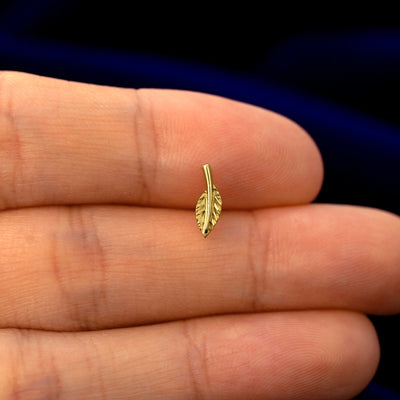 A model holding a solid gold Leaf stud earring between two fingers