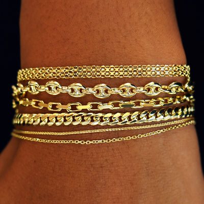 A model's wrist wearing  yellow gold Bismarck, Anchor, Anchor, Medium Miami, Wheat, and Medium Cable Bracelets