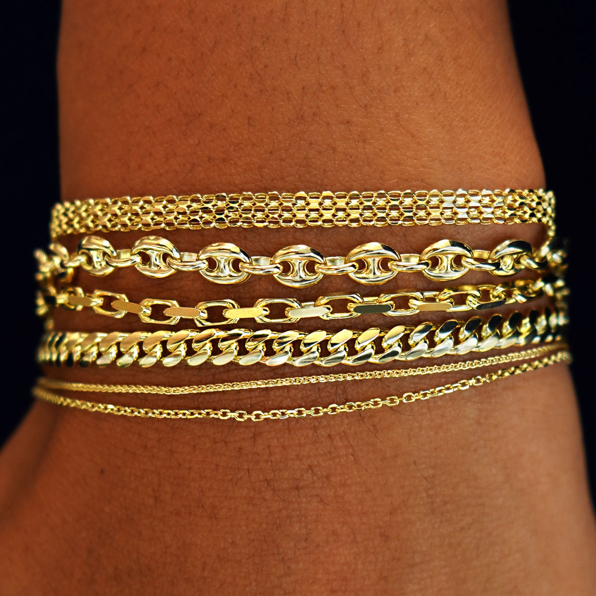 A  model's wrist wearing  yellow gold Bismarck, Puffy Mariner, Anchor, Medium Miami, Wheat, and Medium Cable Bracelets