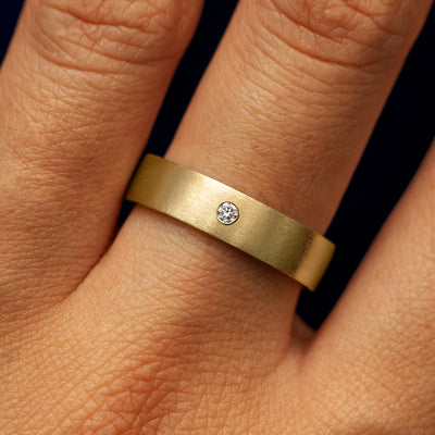 Close up view of a model's fingers wearing a 14k yellow gold Industrial Matte Band with one diamond