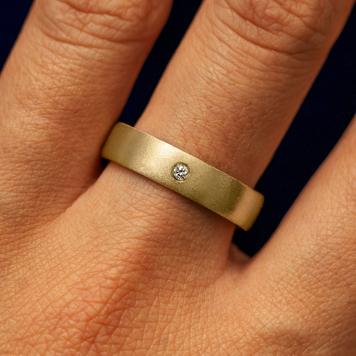 Close up view of a model's fingers wearing a 14k yellow gold Mix Matte Band with one diamond