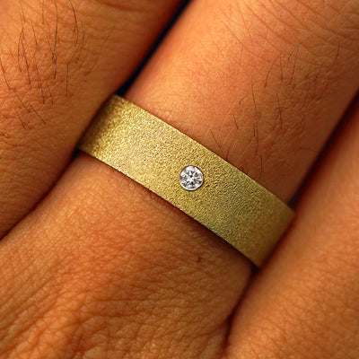 Close up view of a model's fingers wearing a 14k yellow gold Industrial Stardust Band with one diamond