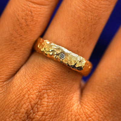 Close up view of a model's fingers wearing a 14k yellow gold Organic Band with one diamond