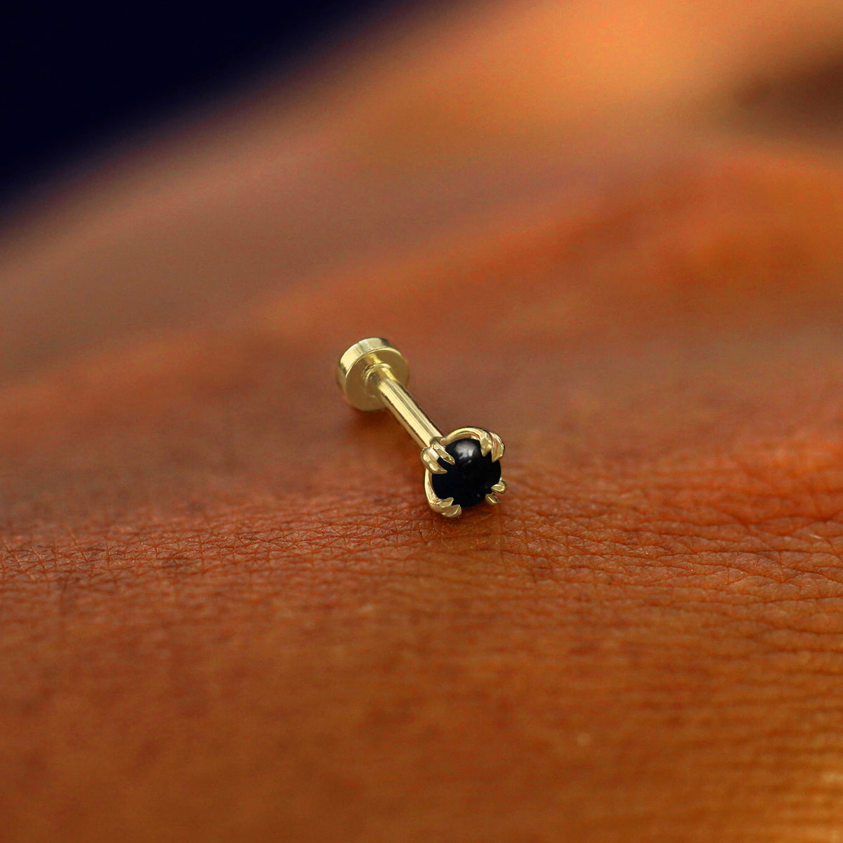 A solid 14k yellow gold Onyx Flatback Piercing resting on the back of a model's hand