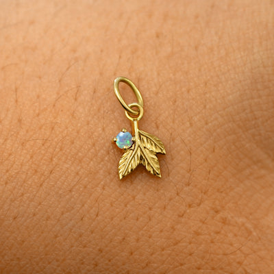 A solid 14k yellow gold opal Gemstone 3 Leaves Charm resting on the back of a model's hand