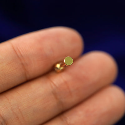 A solid yellow gold Opal Flatback Piercing laying facedown on a model's finger to show the end of the flat back