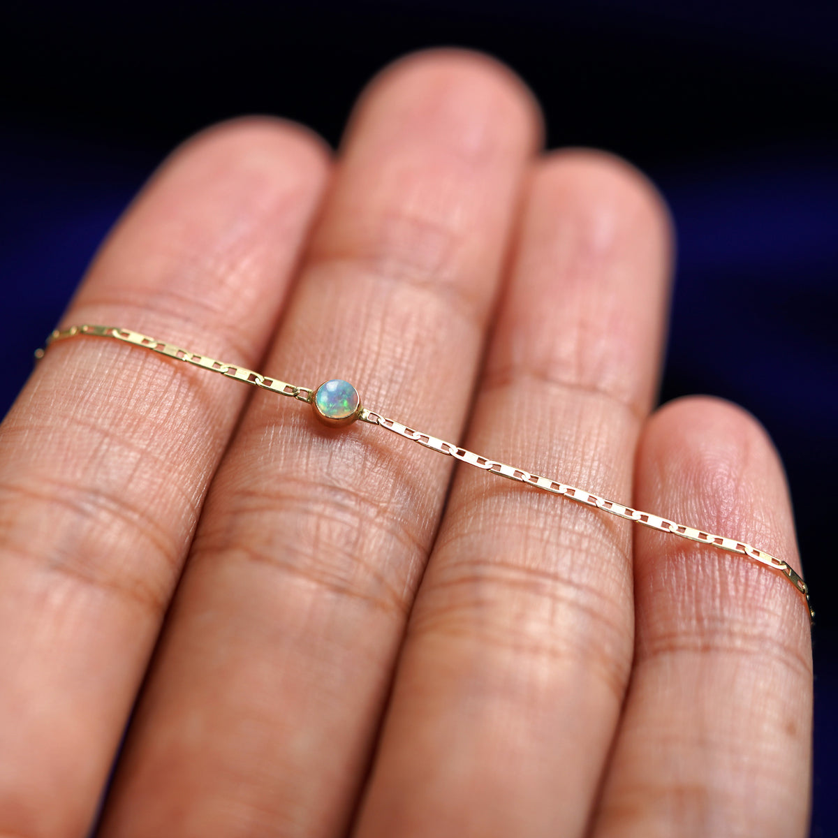 A yellow gold Opal Bracelet resting on a model's fingers