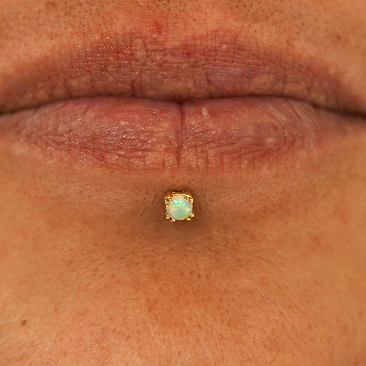 Close up view of a model's lips wearing a 14k yellow gold Opal Flatback in a labret piercing