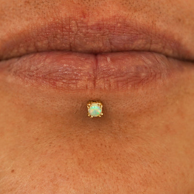 Close up view of a model's lips wearing a 14k yellow gold Opal Flatback in a labret piercing