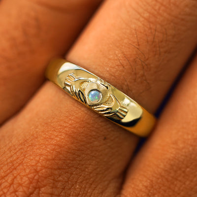 Close up view of a model's fingers wearing a 14k yellow gold opal Gemstone Claddagh Band