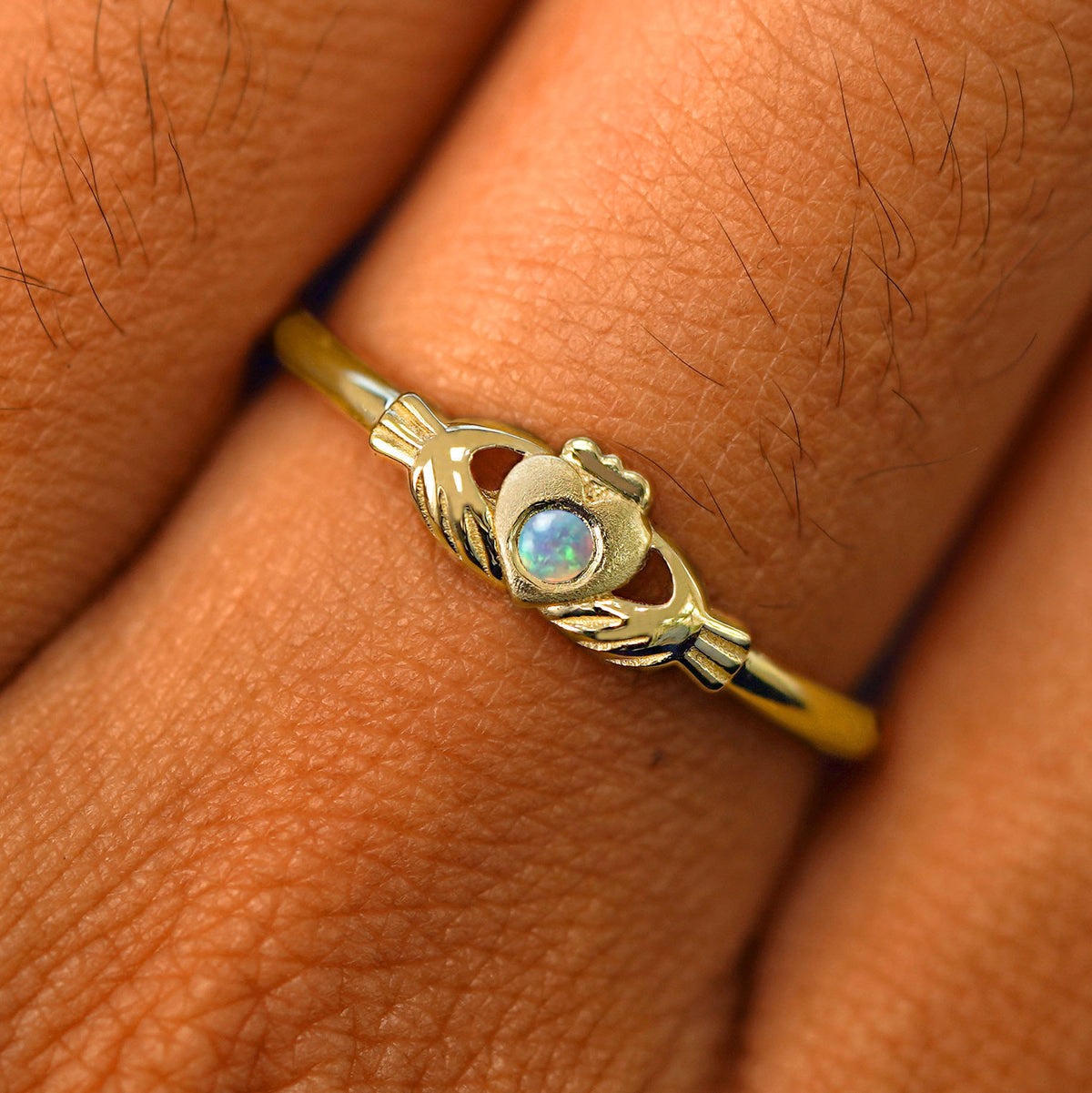 Close up view of a model's fingers wearing a 14k yellow gold opal Thin Gemstone Claddagh Ring