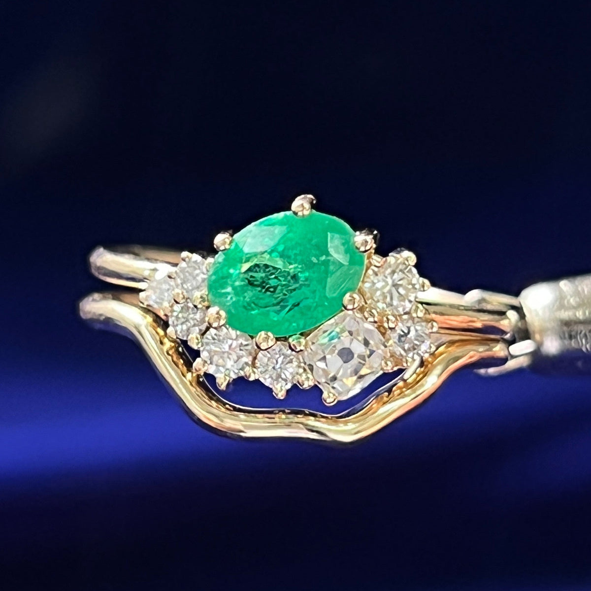 Gold ring with emerald and diamonds on a blue fabric background